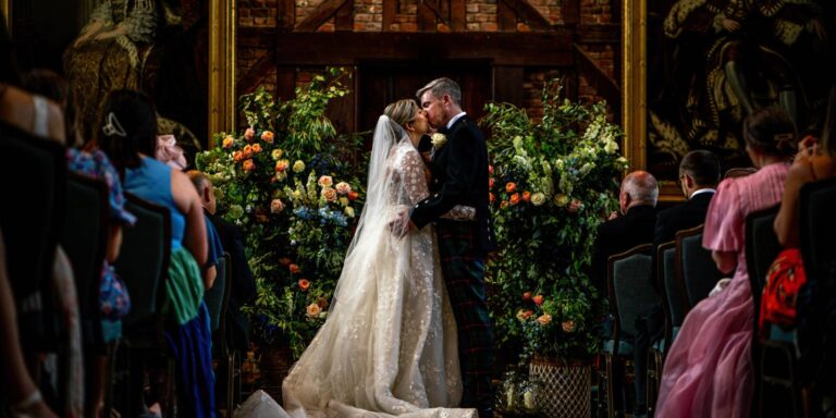 A couple kissing beneath a floral arch during a ceremony, Hatfield House