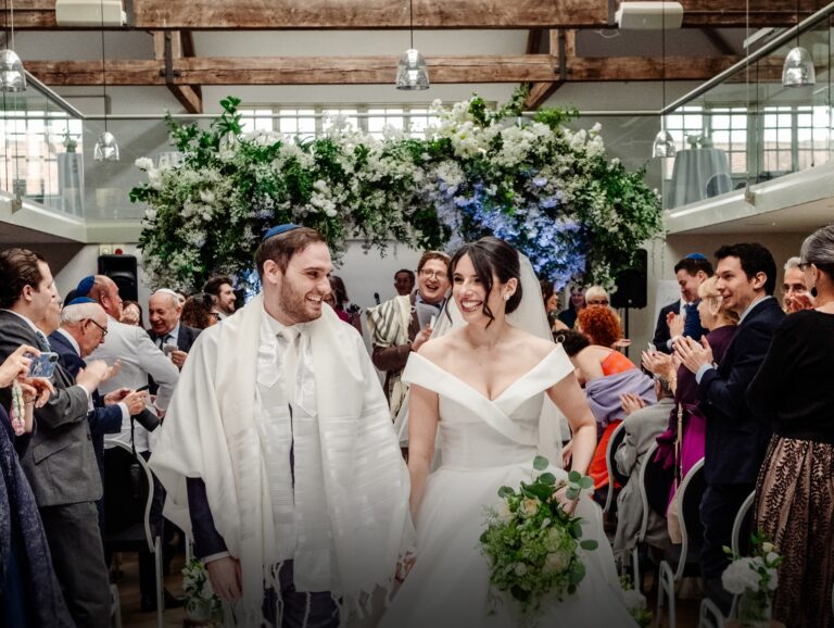 A couple leaving a ceremony beneath a floral canopy, Hatfield House