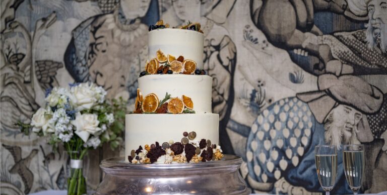 A wedding cake and flowers against a patterned wall hanging, Hatfield House