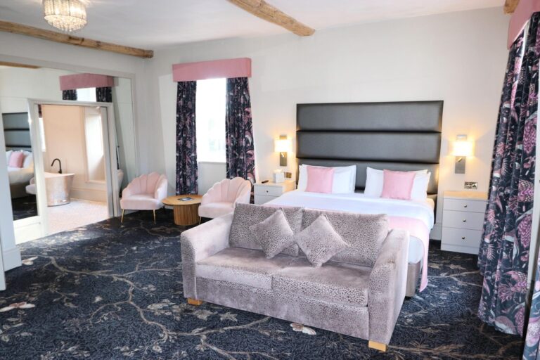 A bridal suite with beamed ceiling, sofa, pink accents and a freestanding bath in the adjoining bathroom, Haycock Manor