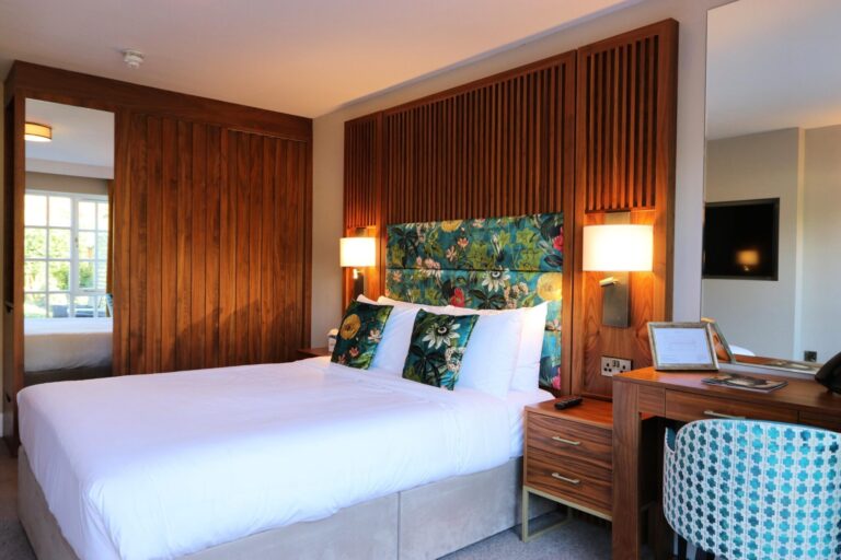 A double bedroom with a walnut-panelled wall, botanical headboard and writing desk, Haycock Manor