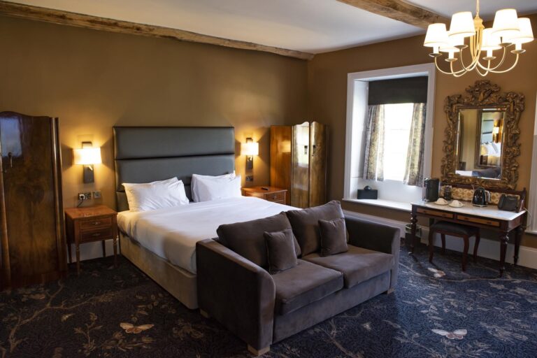 A bedroom in the older part of the hotel with a chandelier, gilt mirror, sofa and beamed ceiling, Haycock Manor