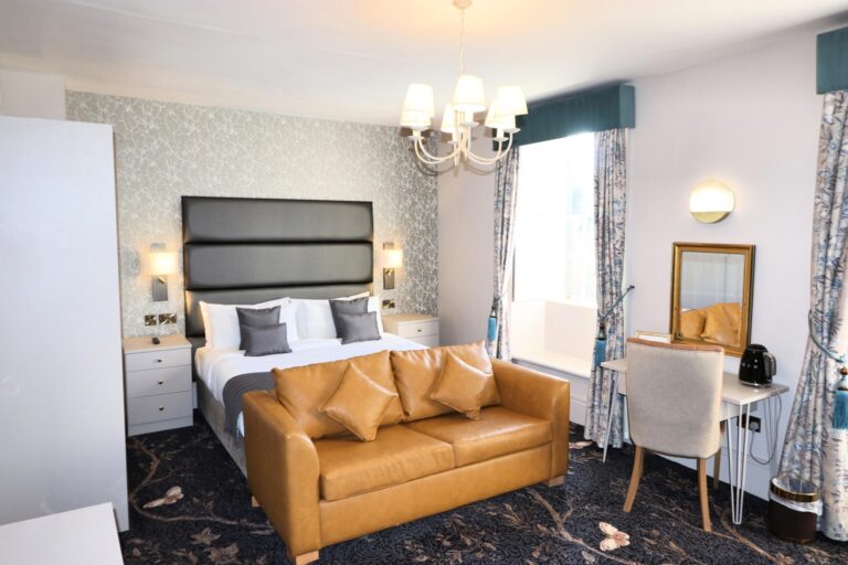 A bedroom with a tan leather sofa, chandelier and patterned curtains, Haycock Manor