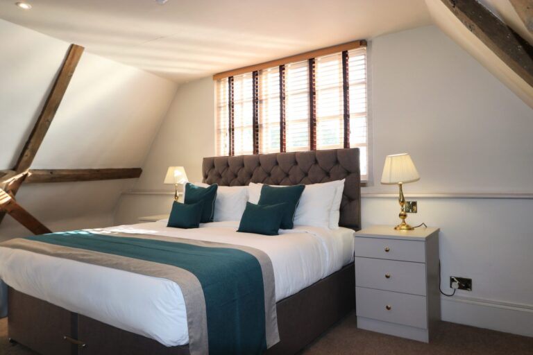 A double room under sloping beamed eaves with a buttoned headboard, Haycock Manor