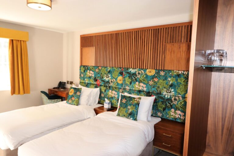 A twin room with a shared botanical headboard and walnut joinery, Haycock Manor