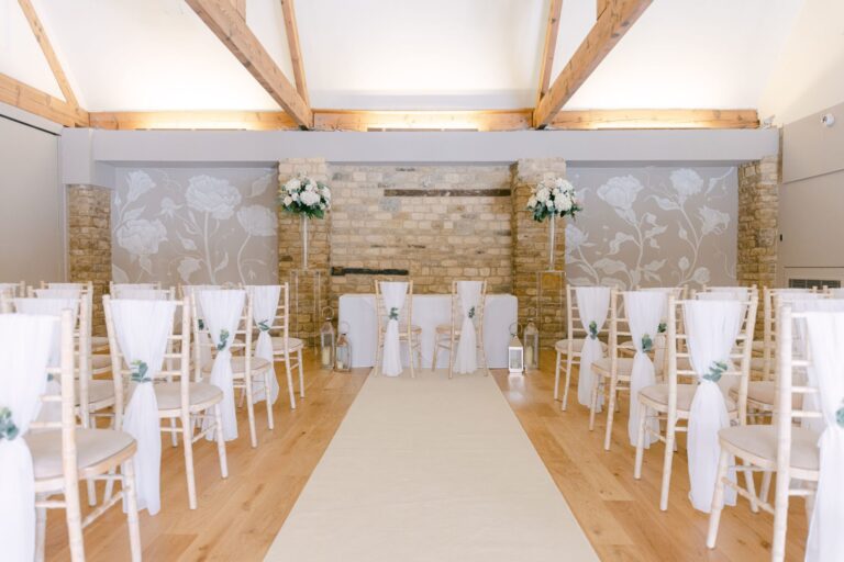 The Manor Suite set for a civil ceremony, with an aisle between dressed chairs under exposed roof trusses, Haycock Manor