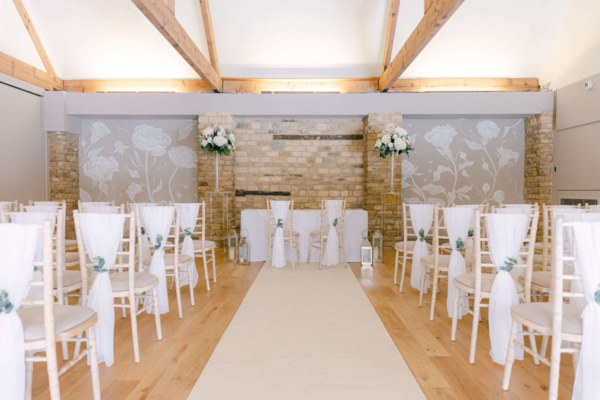 The Manor Suite set for a civil ceremony, with an aisle between dressed chairs under exposed roof trusses, Haycock Manor
