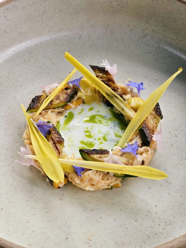 A plated risotto finished with petals and shards of crisp vegetable, Haycock Manor
