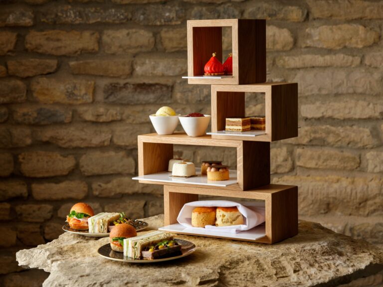 Afternoon tea served on stacked wooden stands against a limestone wall, Haycock Manor