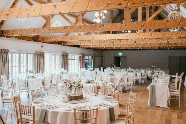 The Haycock Suite laid with round tables for a wedding breakfast beneath fairy-lit oak trusses, Haycock Manor