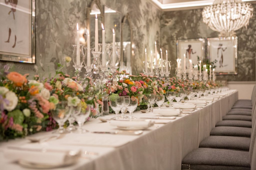 A long table set with flowers and candles against papered walls