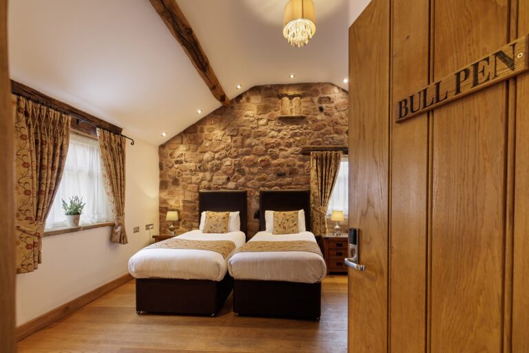 The Bull Pen twin room, with a stone gable wall, beams and a chandelier, Heaton House Farm