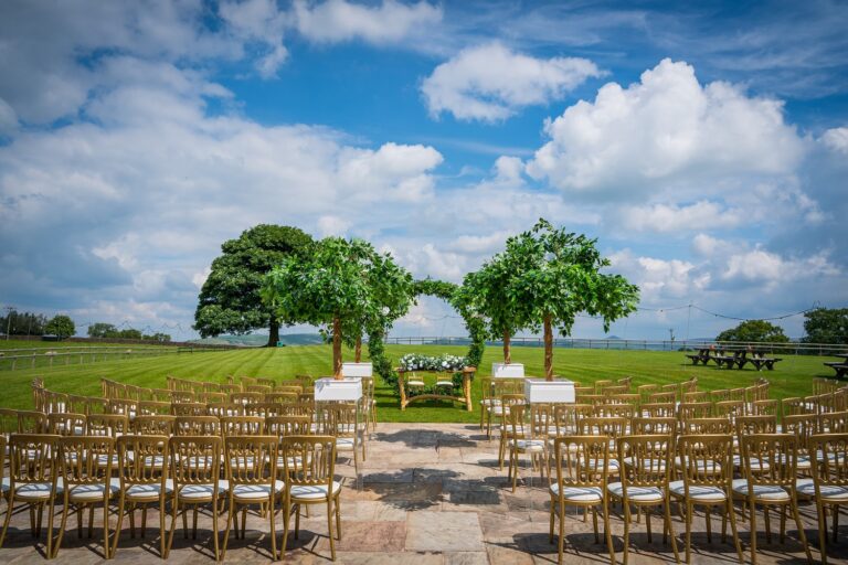 Outdoor ceremony set on the lawn facing the sycamore tree, with rows of gold chairs and open countryside, Heaton House Farm
