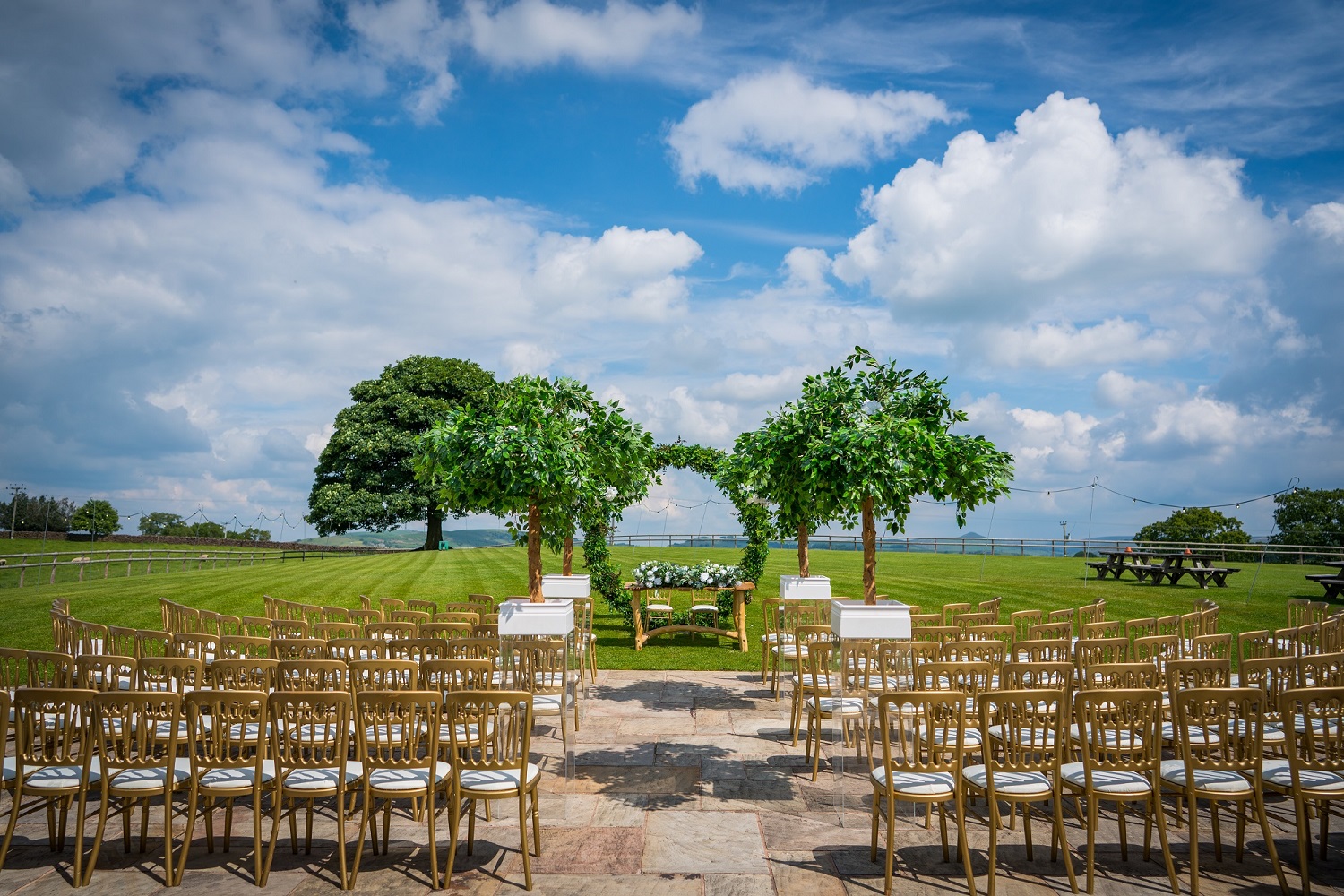 Outdoor ceremony set on the lawn facing the sycamore tree, with rows of gold chairs and open countryside, Heaton House Farm
