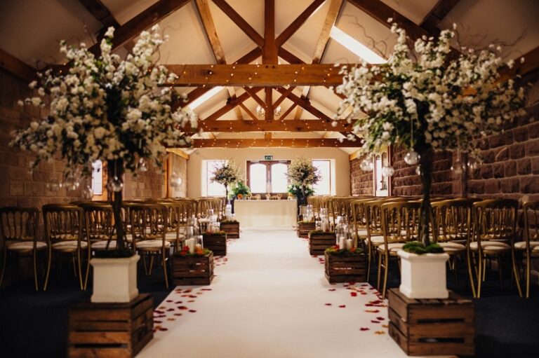 The Oak Beamed Barn set for a ceremony, with sandstone walls, exposed oak trusses and blossom trees along the aisle, Heaton House Farm