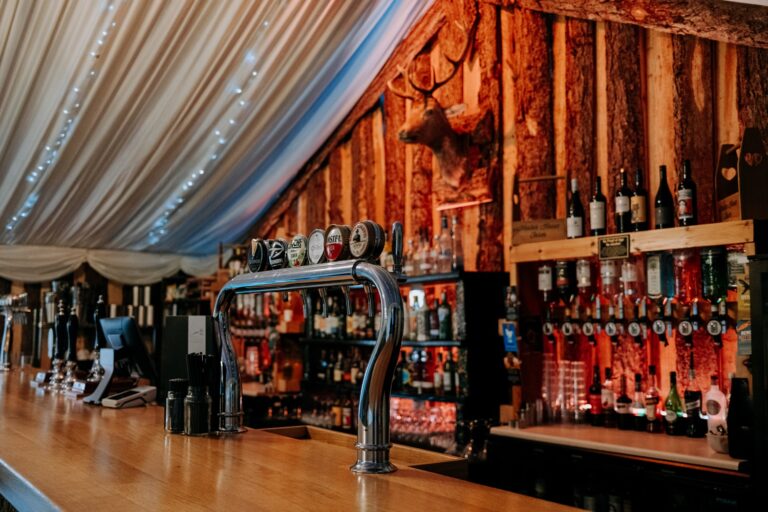 The bar, with hand pumps, a mounted stag head and timber cladding under the ceiling drapes, Heaton House Farm
