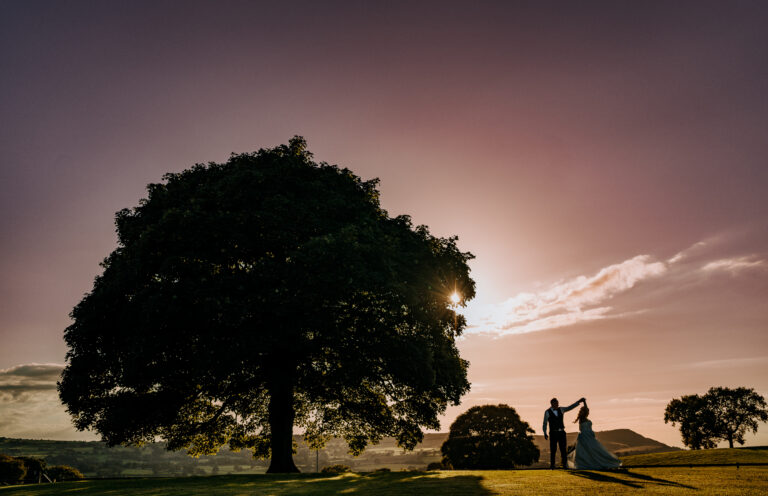 Couple silhouetted beneath the lone sycamore tree on the hillside at dusk, Heaton House Farm