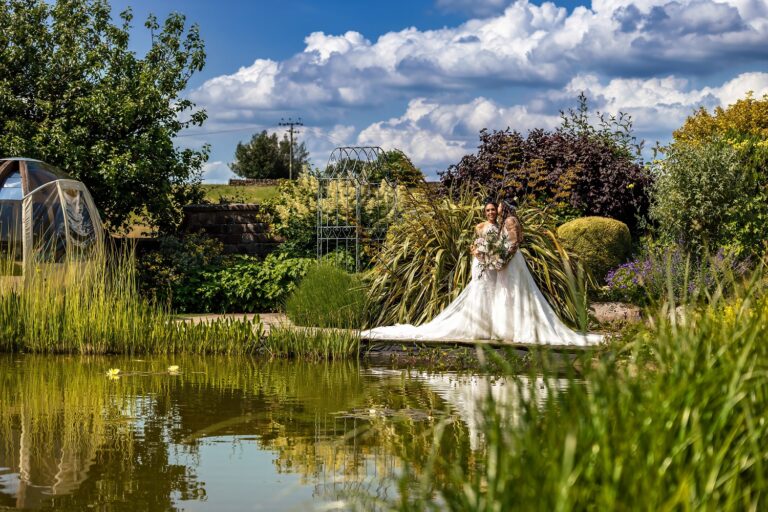 The pond in the water gardens, fringed with reeds and planting, with a bride by the water, Heaton House Farm