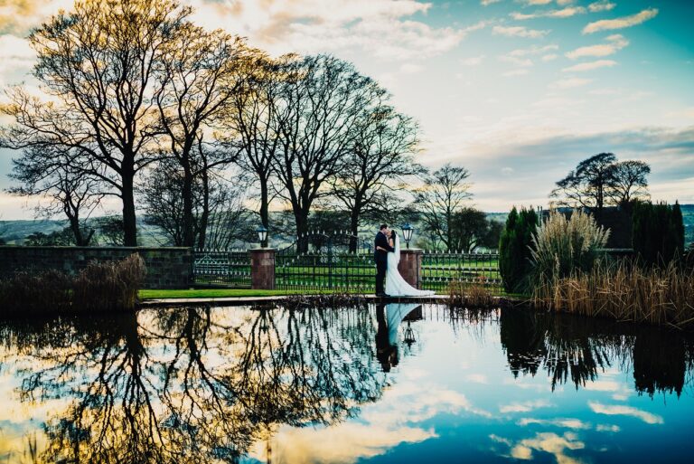 A couple reflected in still water beneath bare trees in late light, Heaton House Farm