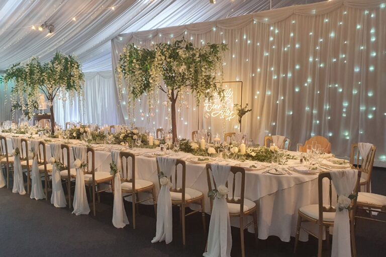A long top table dressed with greenery in front of a twinkling curtain backdrop, Heaton House Farm