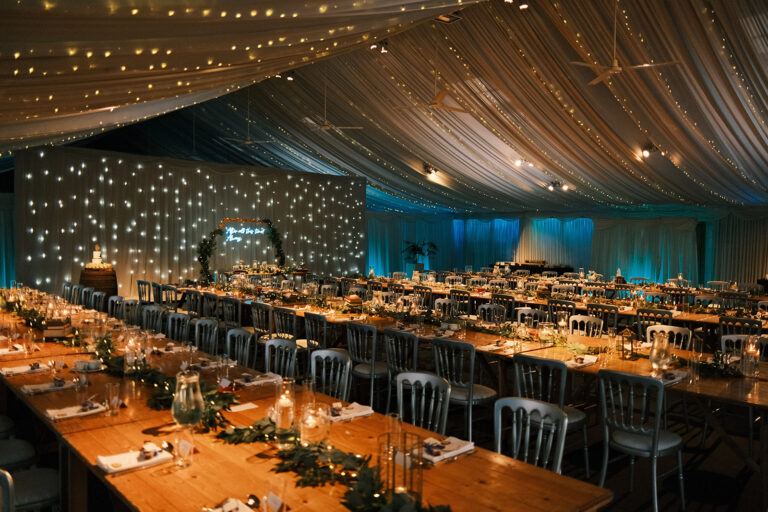Long wooden banqueting tables under festoon lights with a starlit wall at the far end, Heaton House Farm