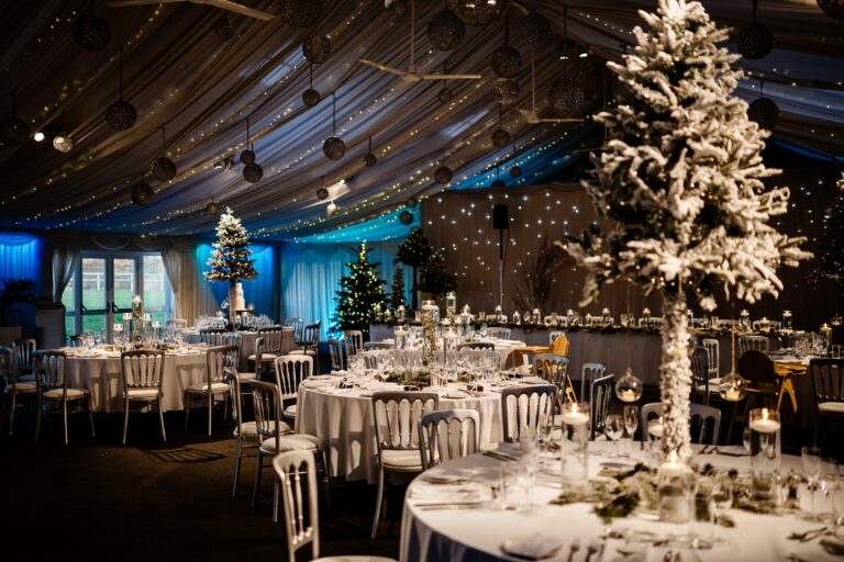 The dining barn set for a winter wedding with snow-dusted Christmas trees and blue uplighting, Heaton House Farm