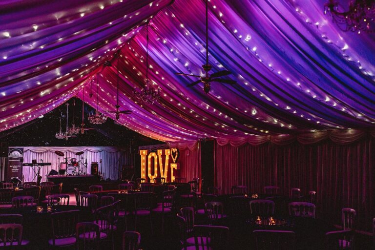 The Wedding Barn in the evening, its draped ceiling lit purple and pink, with light-up LOVE letters by the stage, Heaton House Farm