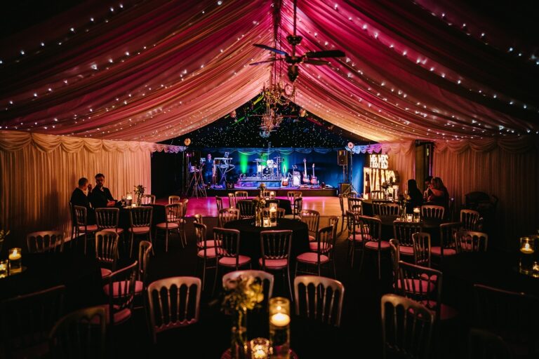 The Wedding Barn with a band on the stage, fairy lights in the pink-lit ceiling drapes, Heaton House Farm