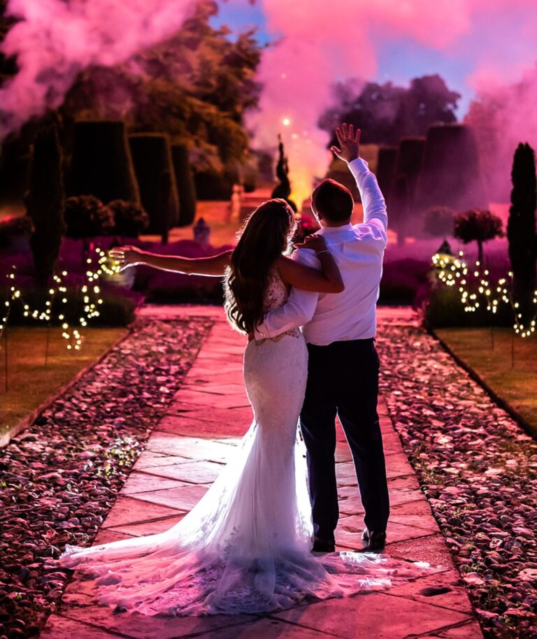 A couple at dusk on a petal-strewn path, lit by rose-coloured smoke, Hengrave Hall