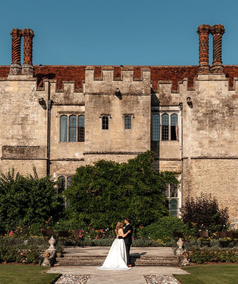 A couple embrace before the crenellated stone tower of the hall, Hengrave Hall