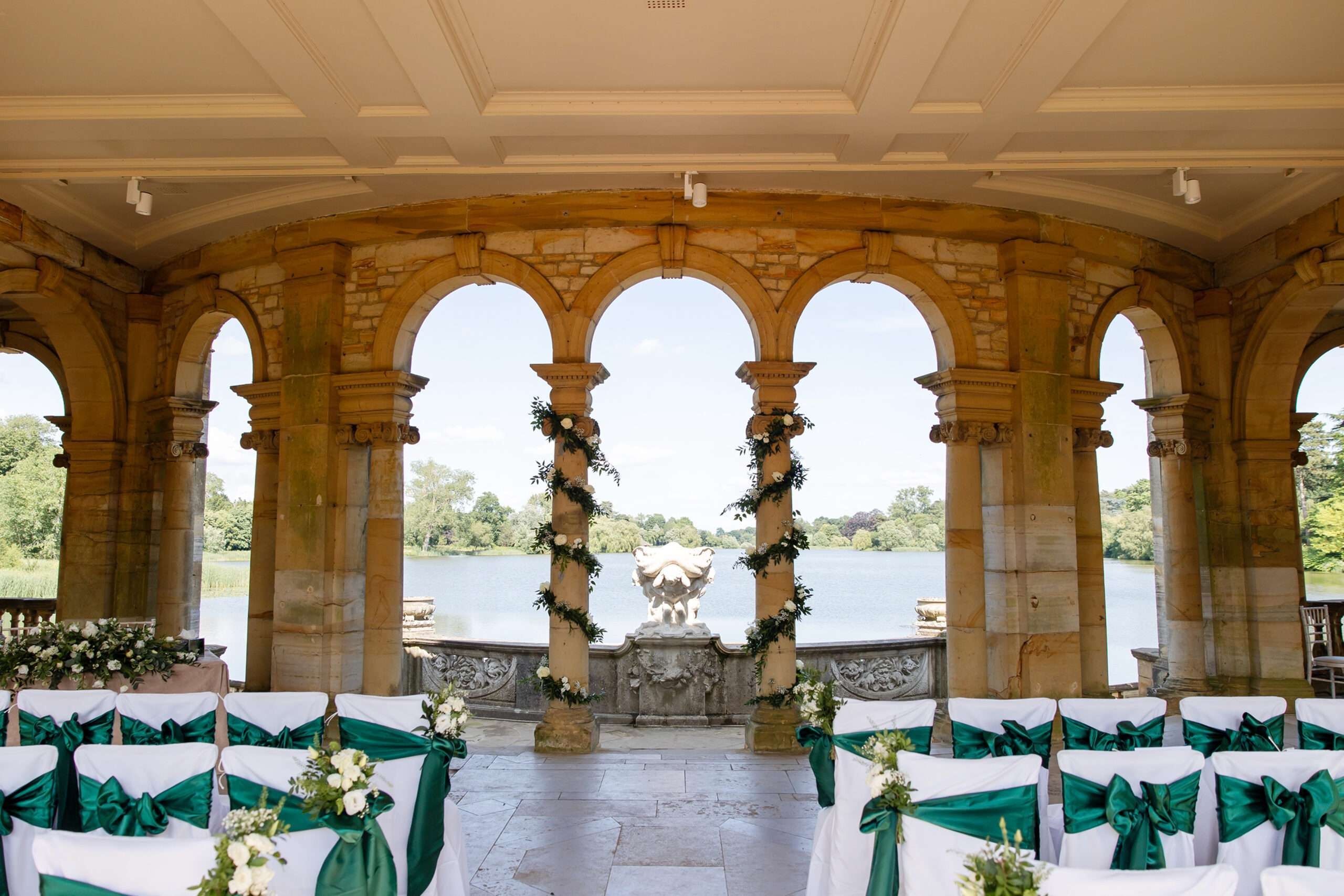 The Loggia in the Italian Garden dressed for a ceremony, stone columns and chairs with green sashes above the lake, Hever Castle