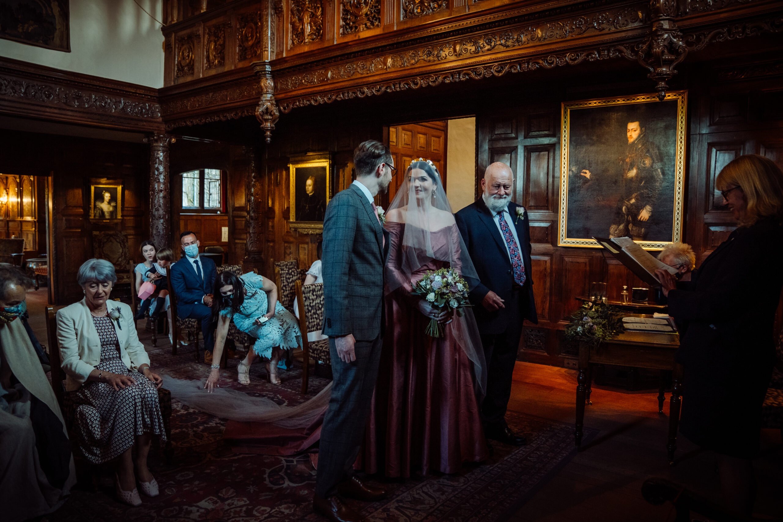 A ceremony in a dark-panelled room of the castle, the bride walking in on an arm before seated guests, Hever Castle