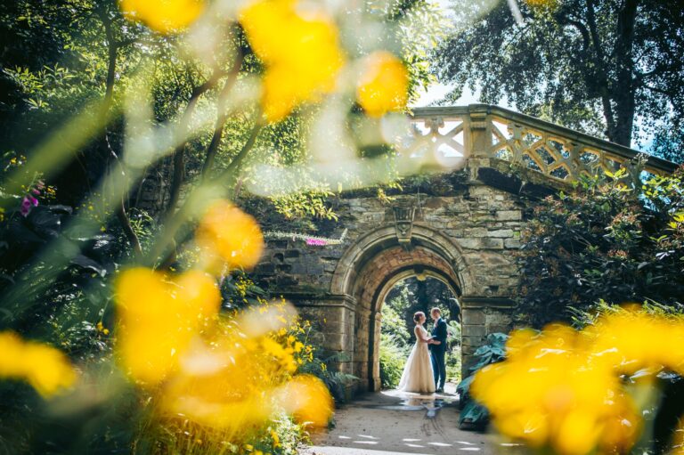 A couple kissing beneath a stone garden archway, framed by yellow flowers, Hever Castle