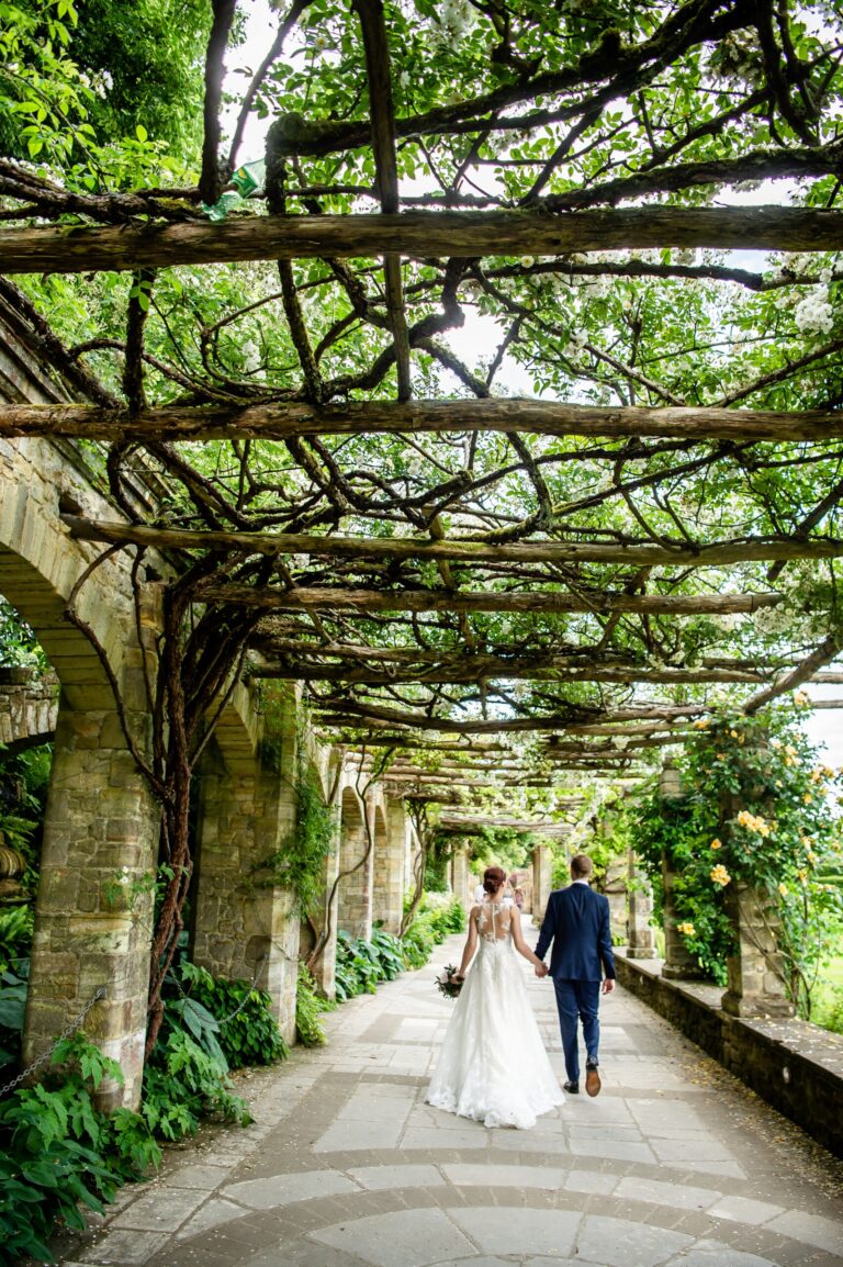 A couple walking hand in hand beneath the wisteria-clad pergola of the Italian Garden, Hever Castle