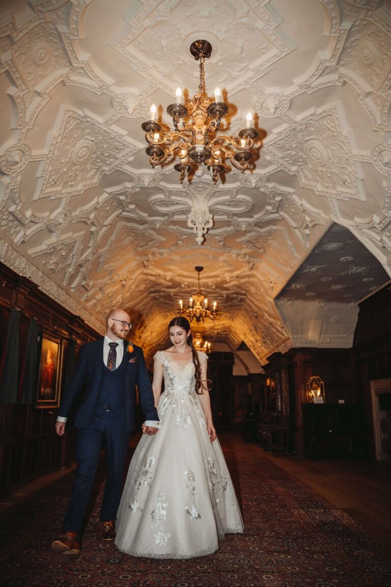 A couple beneath the ornate carved plaster ceiling and chandeliers of the castle Long Gallery, Hever Castle