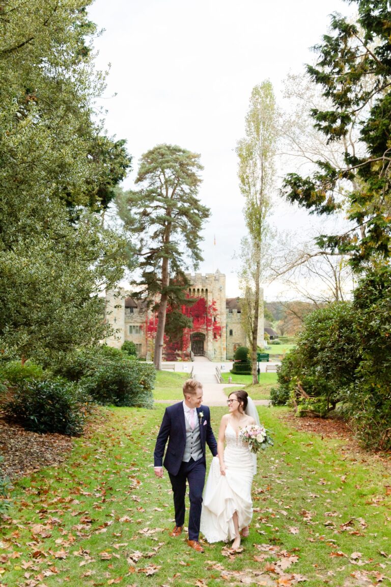 A couple walking a garden path with the castle rising beyond in autumn, Hever Castle