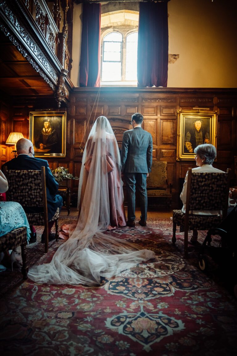 A bride in a long veil and her groom before a mullioned window in a panelled room of the castle, Hever Castle