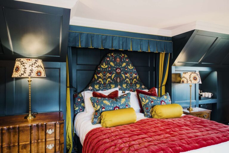 A bed and breakfast bedroom with deep teal panelling, a floral headboard and a red quilt, Hever Castle