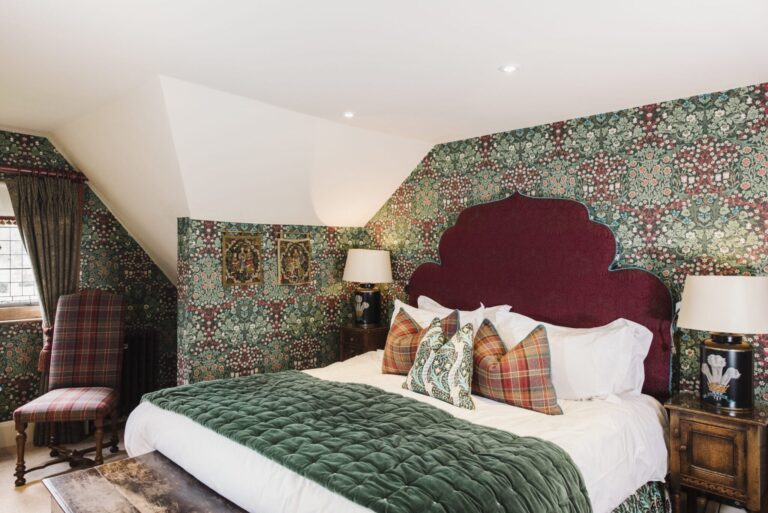 A bedroom with green patterned wallpaper, a burgundy velvet headboard and a tartan armchair, Hever Castle