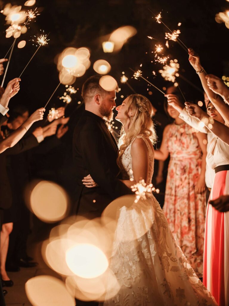 A couple kissing amid guests holding sparklers after dark, Hever Castle