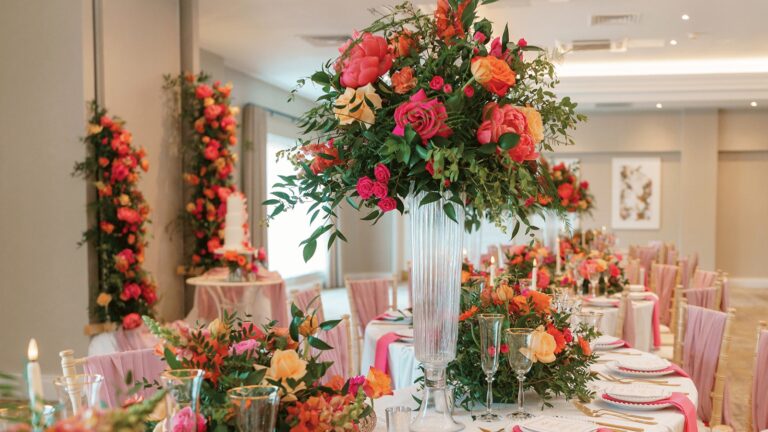A reception room dressed with tall pink and orange flower arrangements and round tables, Horwood House Hotel & Spa