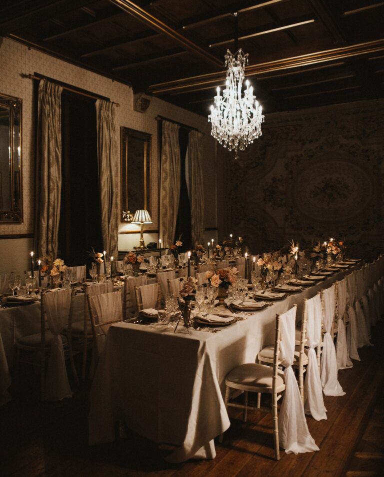 A long table laid for a candlelit wedding breakfast beneath a chandelier, Huntsham Court