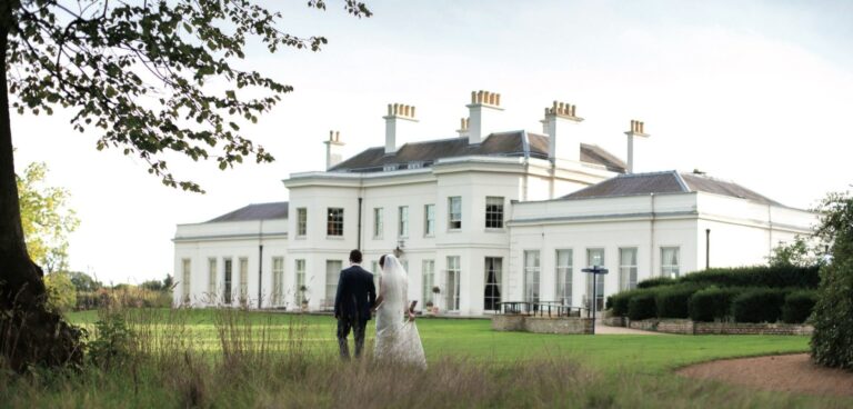 Hylands House across the parkland meadow, a couple on the lawn before the portico, Hylands Estate