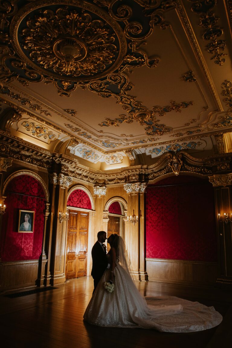 The couple silhouetted in the Banqueting Room, gilded ceiling and red silk above, Hylands Estate