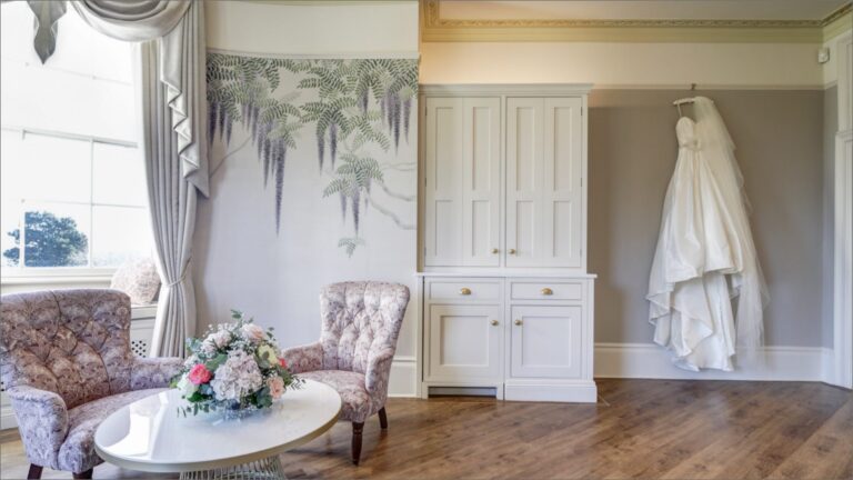 A wedding dress hanging against hand-painted botanical walls in a wedding suite, Hylands Estate