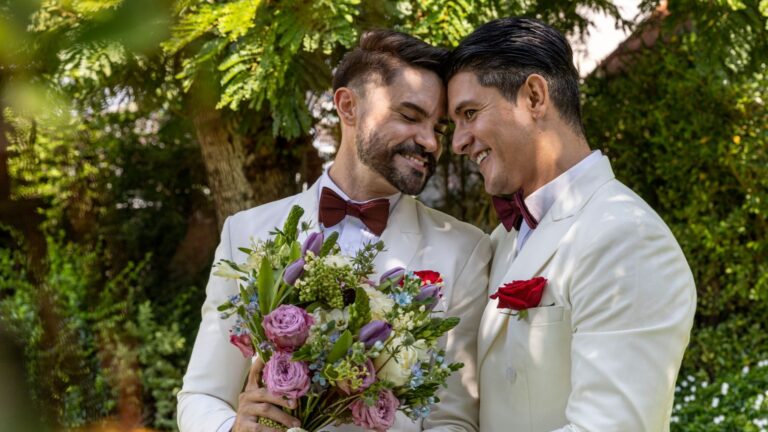 Two grooms with buttonholes and bouquet beneath the trees in the grounds, Hylands Estate