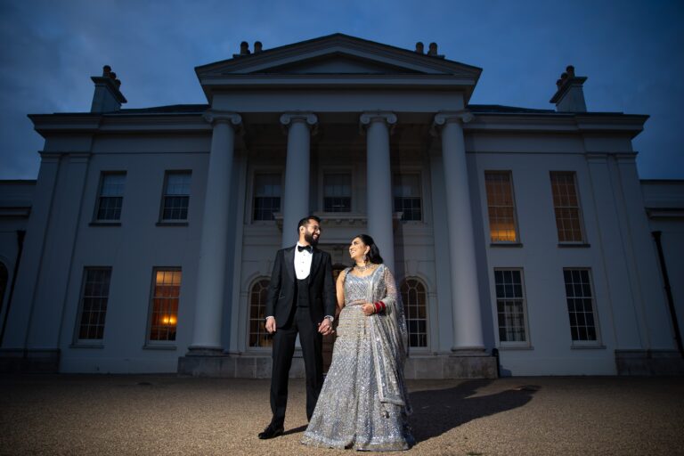 A couple in Indian dress on the front steps, the portico floodlit at dusk, Hylands Estate