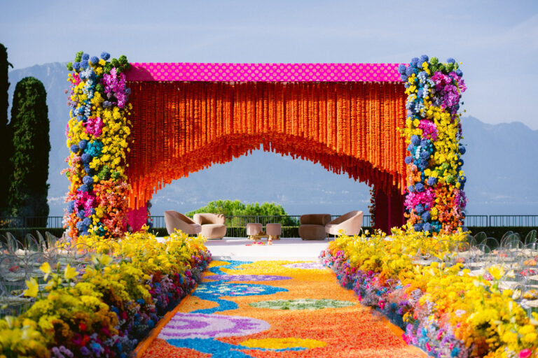 A ceremony frame of orange marigold curtains and bright flower columns above a petal carpet, with mountains beyond, IAMFLOWER