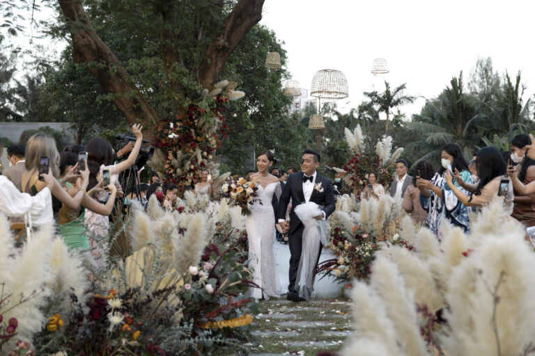 A couple walking out through arrangements of pampas grass and dark dried flowers in a garden, IAMFLOWER