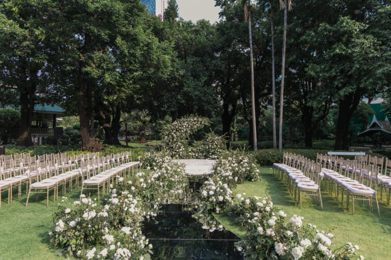 A park ceremony with rows of gold chairs and an aisle of white roses around a reflective pool, IAMFLOWER